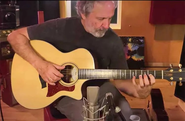 Mark Leggett seated playing an acoustic guitar