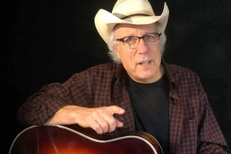 singer-songwriter Maurice Tani seated and holding an acoustic guitar