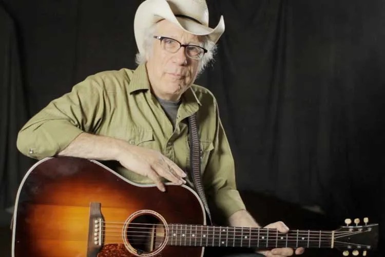 singer-songwriter maurice tani seated holding an acoustic guitar