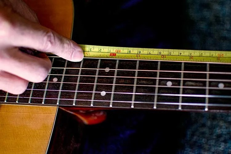 closeup of an acoustic guitar fretboard and a tape measure being used to measure scale length