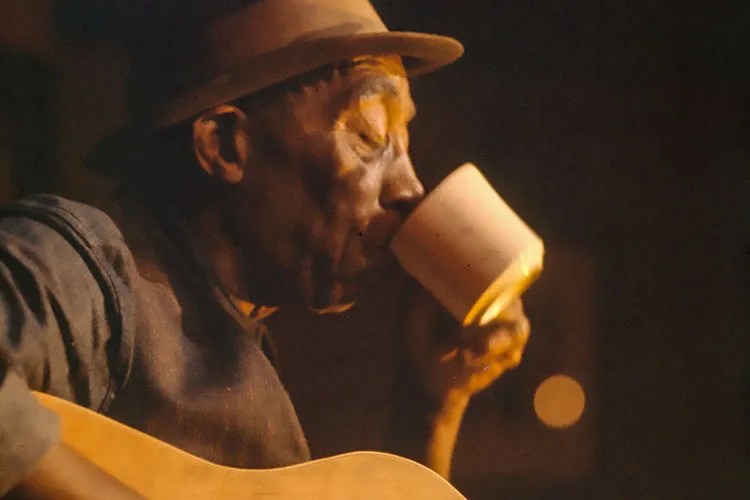 Mississippi John Hurt with guitar drinking coffee