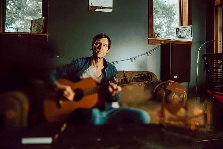 nathan salsburg with acoustic guitar on a couch