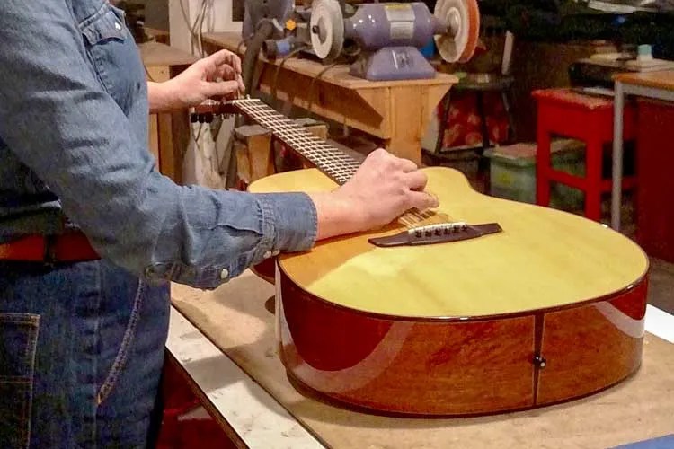 a repair tech making adjustment to an acoustic guitar in a workshop