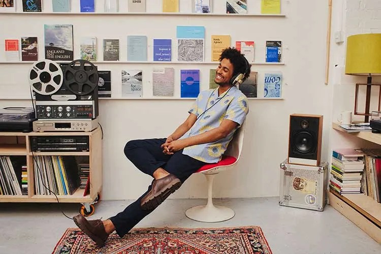 Plinio Fernandes wearing headphones and smiling in a listening library. photo by Lil Eiger