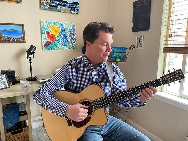 Sean McGowan holding acoustic guitar in his home studio