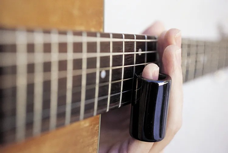 guitar being played with slide on pinky viewed from the soundhole up the neck