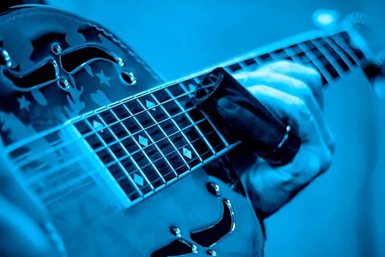 blue tinted photo of acoustic guitar being played with a slide