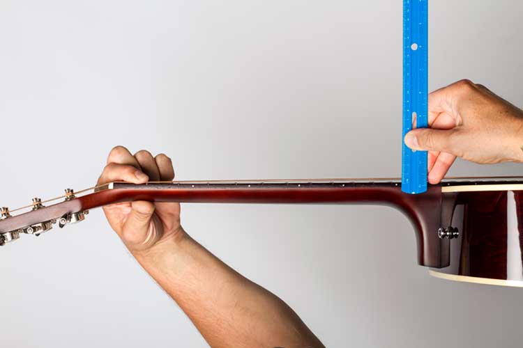 closeup photo of a guitar tech measuring the action on an acoustic guitar