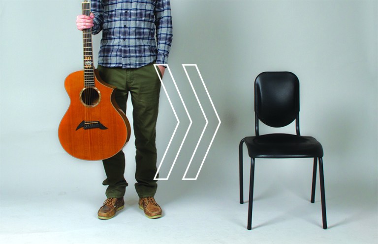 person holds a guitar next to a chair