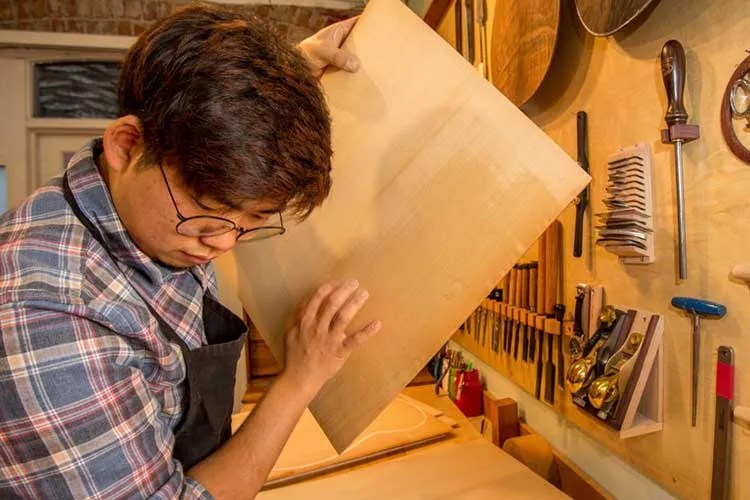 guitar luthier listening to sonic characteristics of tonewood