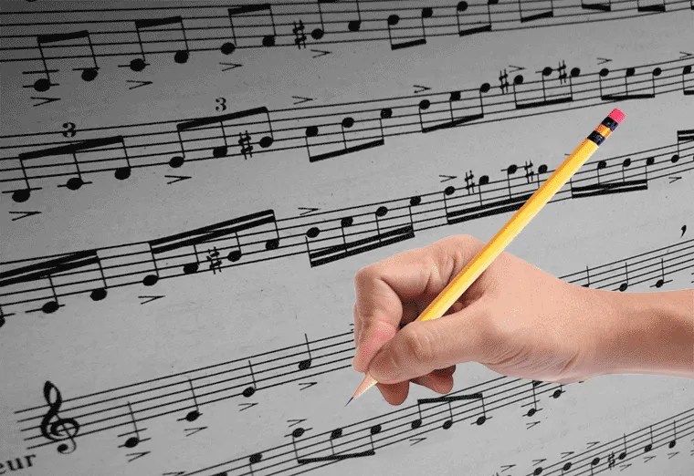 A composer's hand gripping a pencil and preparing to make edits to a musical score