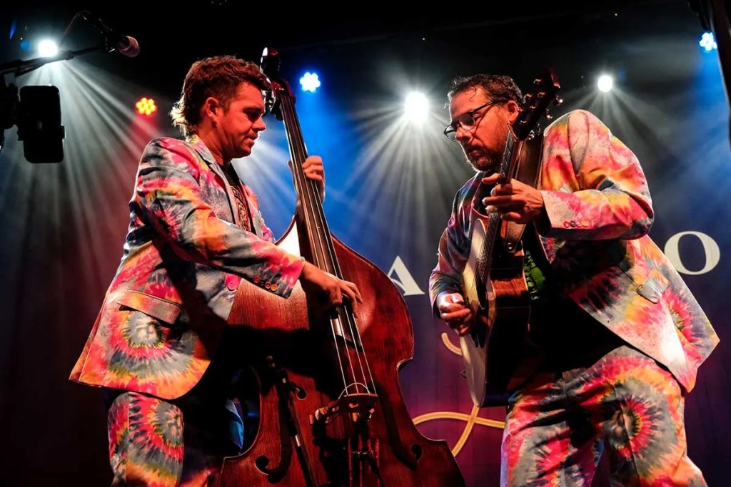 Travis Book and Andy Falco of the Infamous Stringdusters onstage in tie-dye suits.