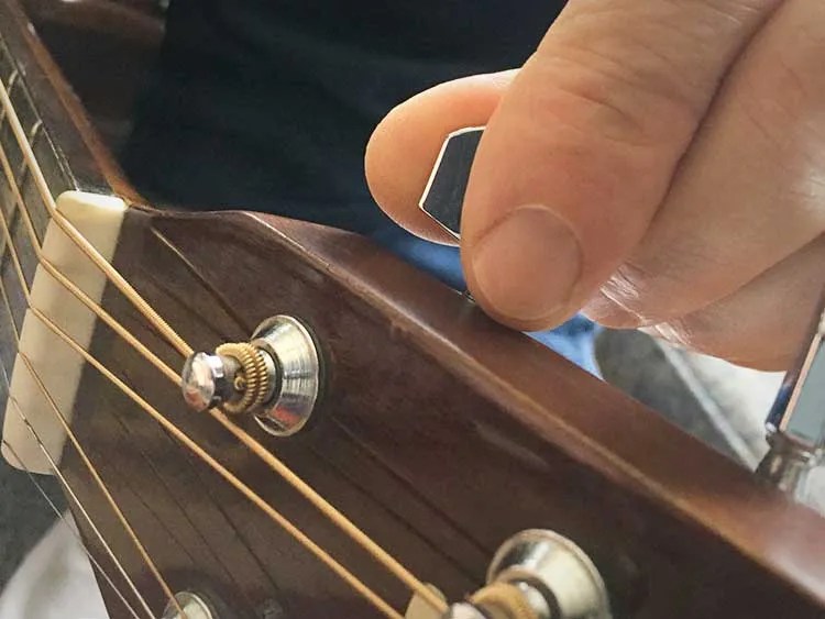 closeup of a guitarist turning the tuning pegs on an acoustic guitar headstock.