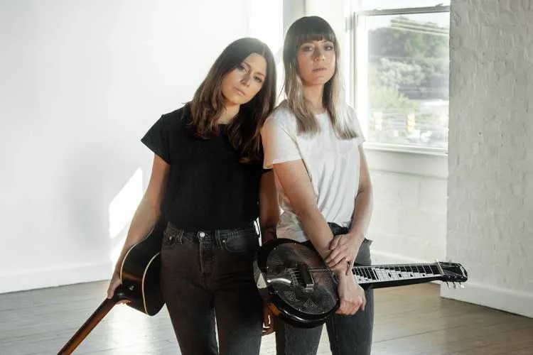 Larkin Poe standing in empty room with guitars