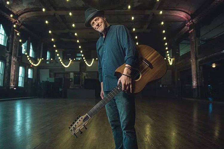 Willy-Porter standing with guitar in hand in an empty concert hall Photo by Cory Zimmerman/Z2