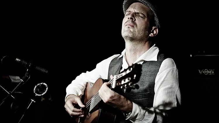 Wolfgang Muthspiel playing a nylon-string guitar onstage in front of a microphone. © Laura Pleifer