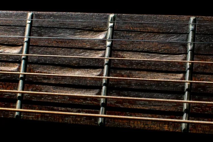 closeup of a scalloped guitar fretboard with worn frets